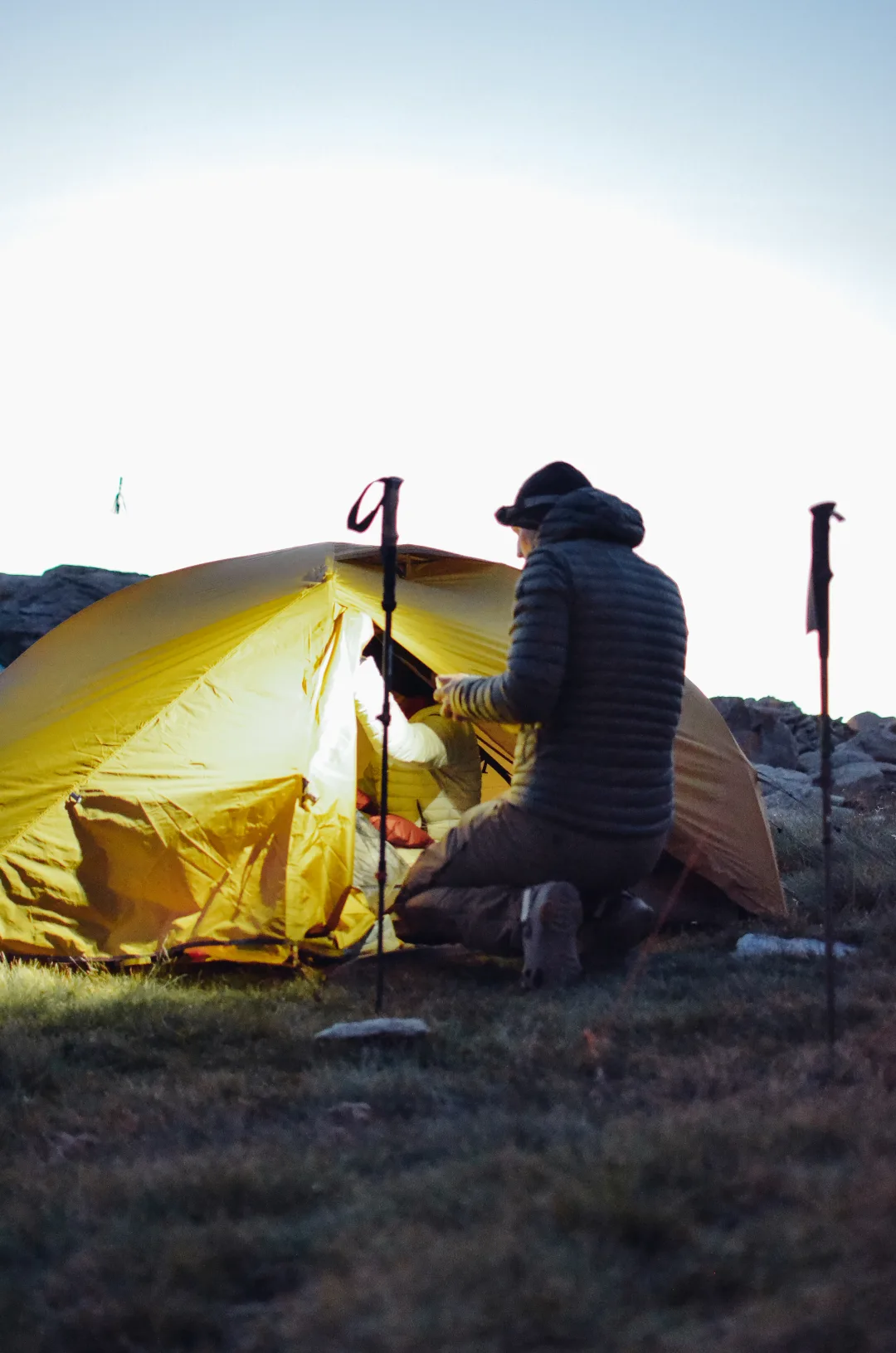 Camper working beside a glowing tent in the mountains
