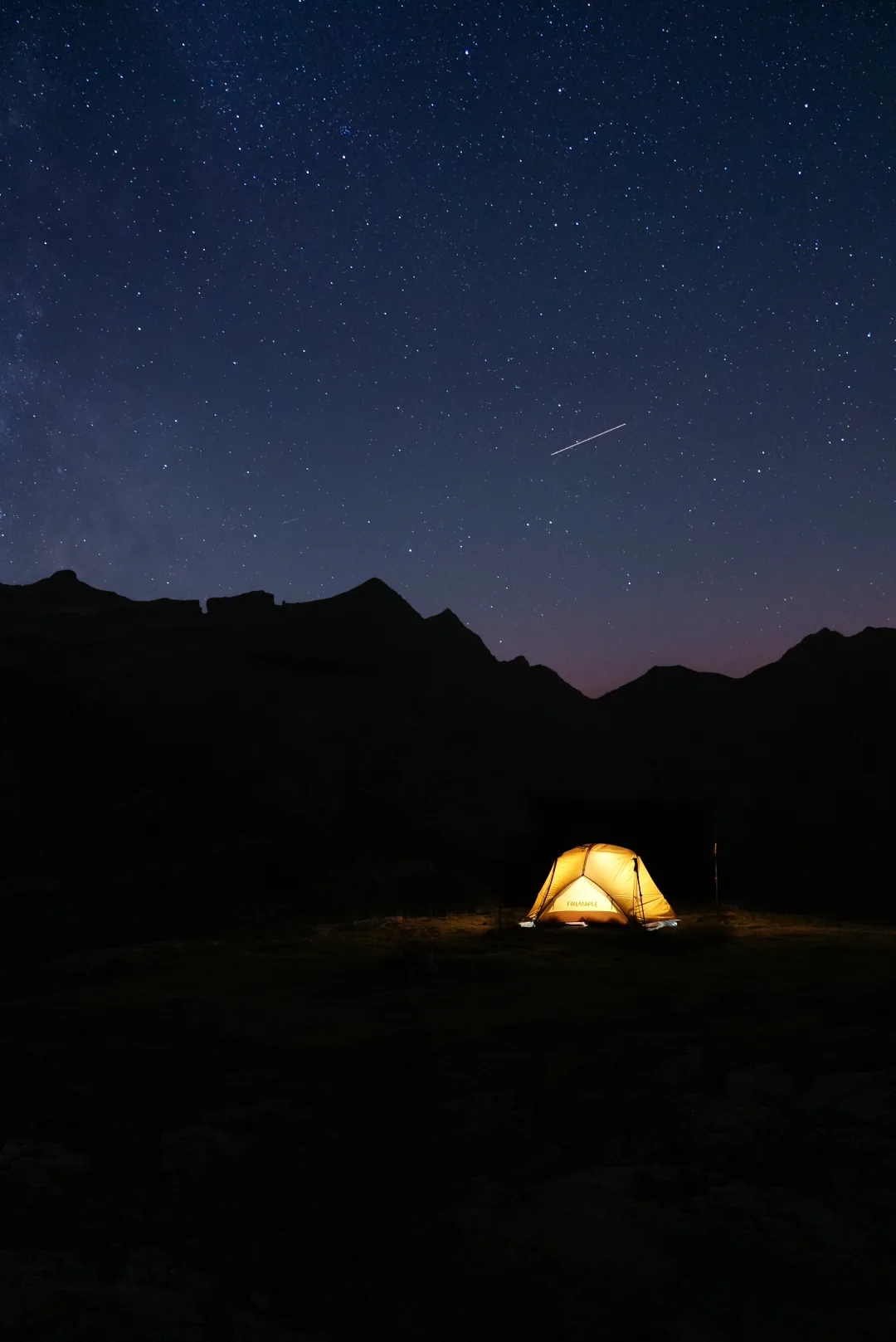 Illuminated mountain tent beneath a star-filled night sky