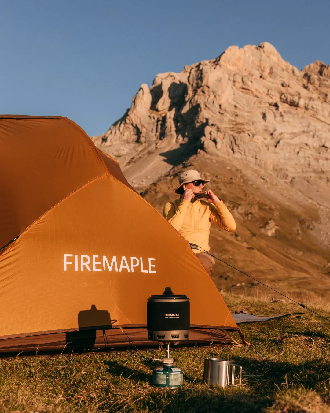 Firemaple stove and orange tent set against a sunlit mountain ridge