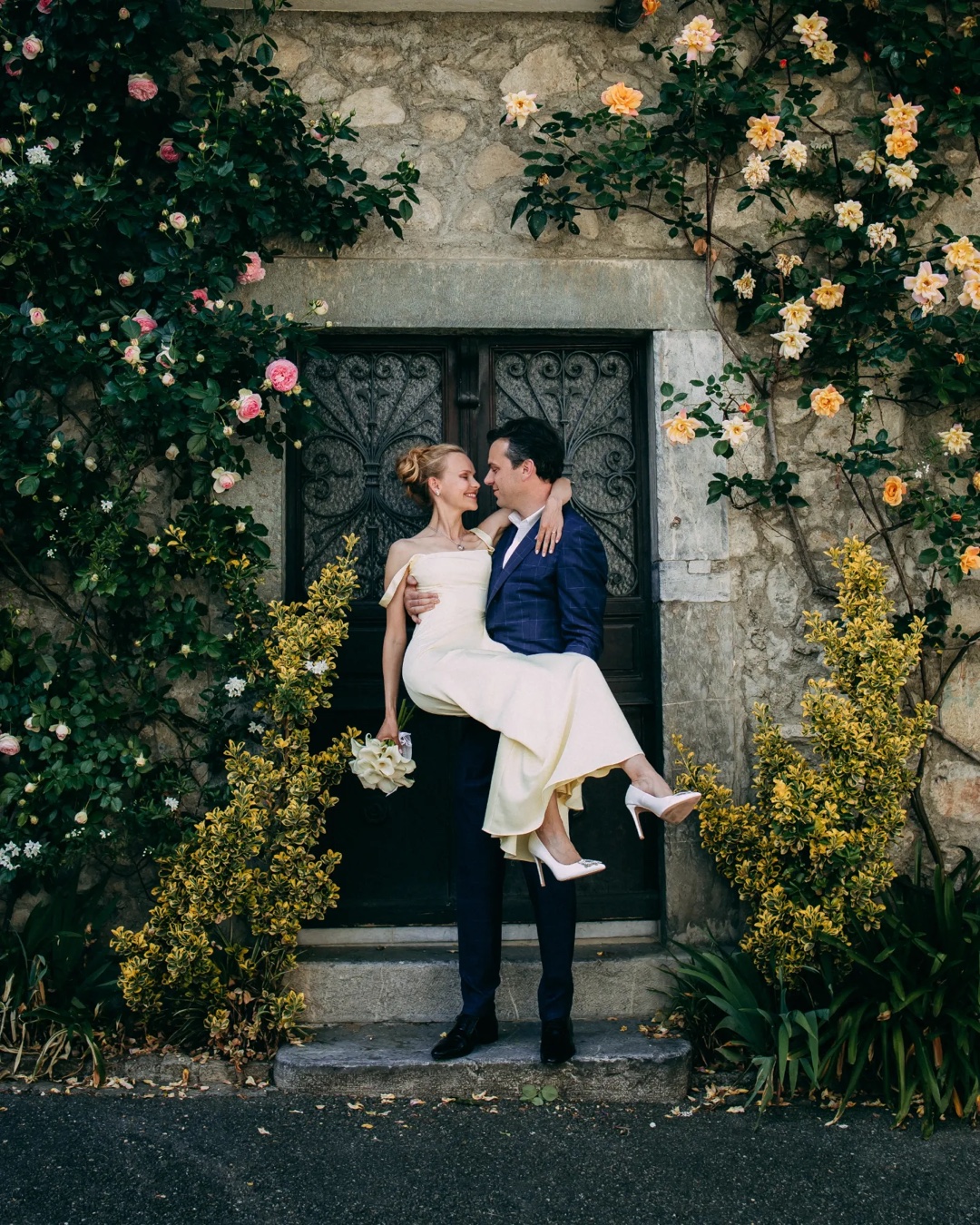 Newly married couple embracing beneath flowers at a stone doorway